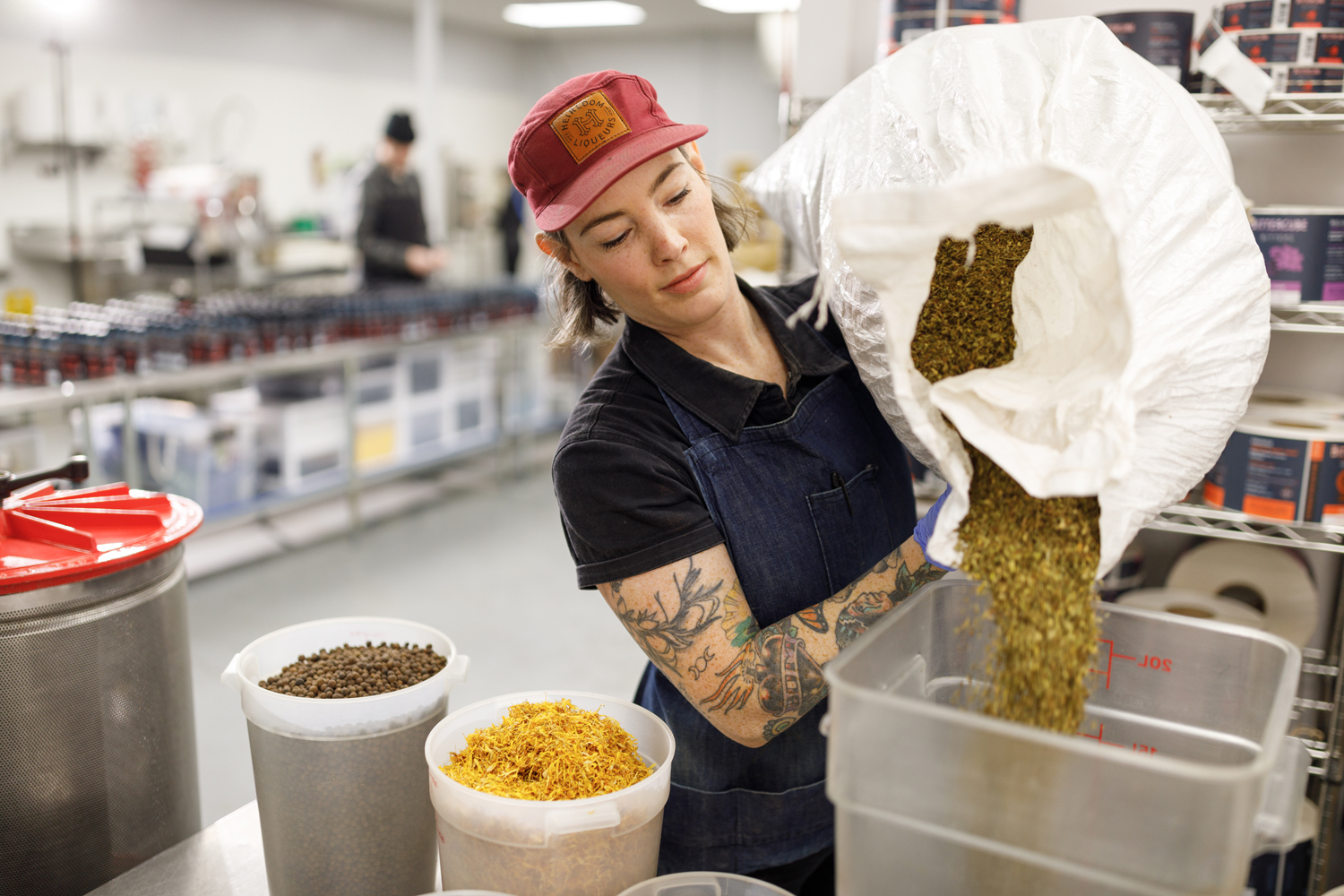 A woman pouring a large bag of spices into another container surounded by bins of spices