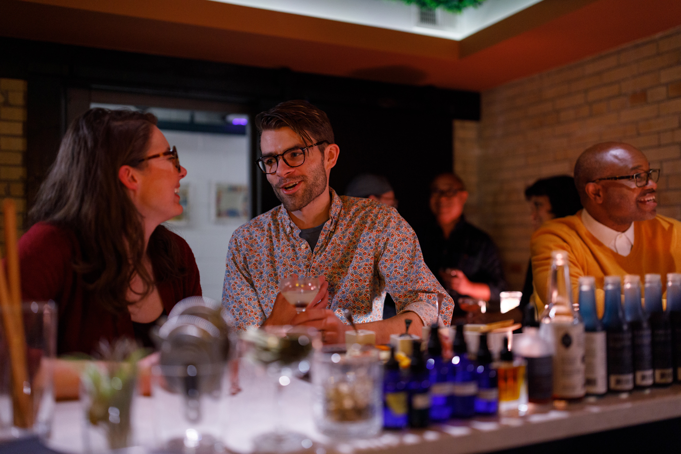 Groups of people sitting at a bar with a row of bitters bottles in front